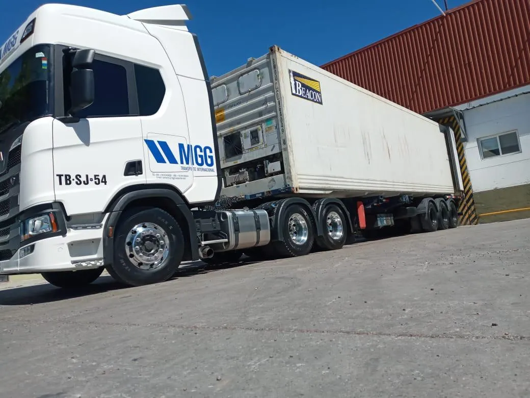 Scania blanco con contenedor frente a un galpón rojo